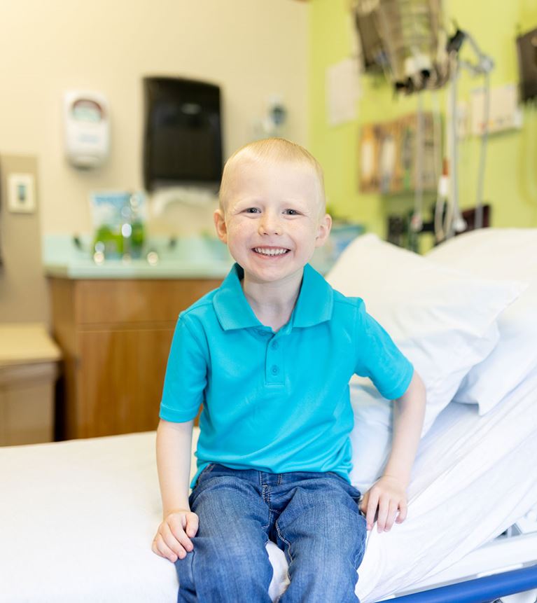 Smiling boy in hospital room wearing a blue shirt.