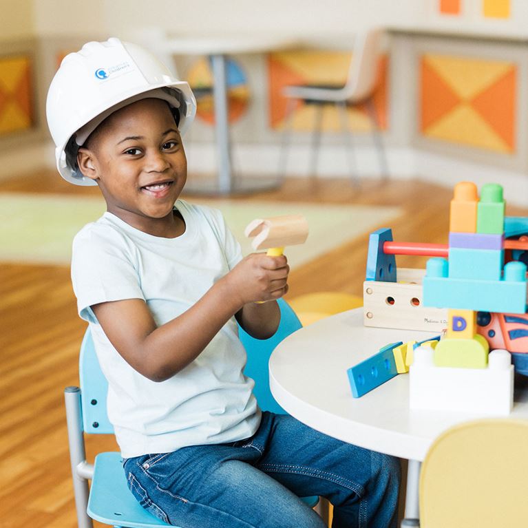 Boy in a playroom wearing white shirt and white construction hat.