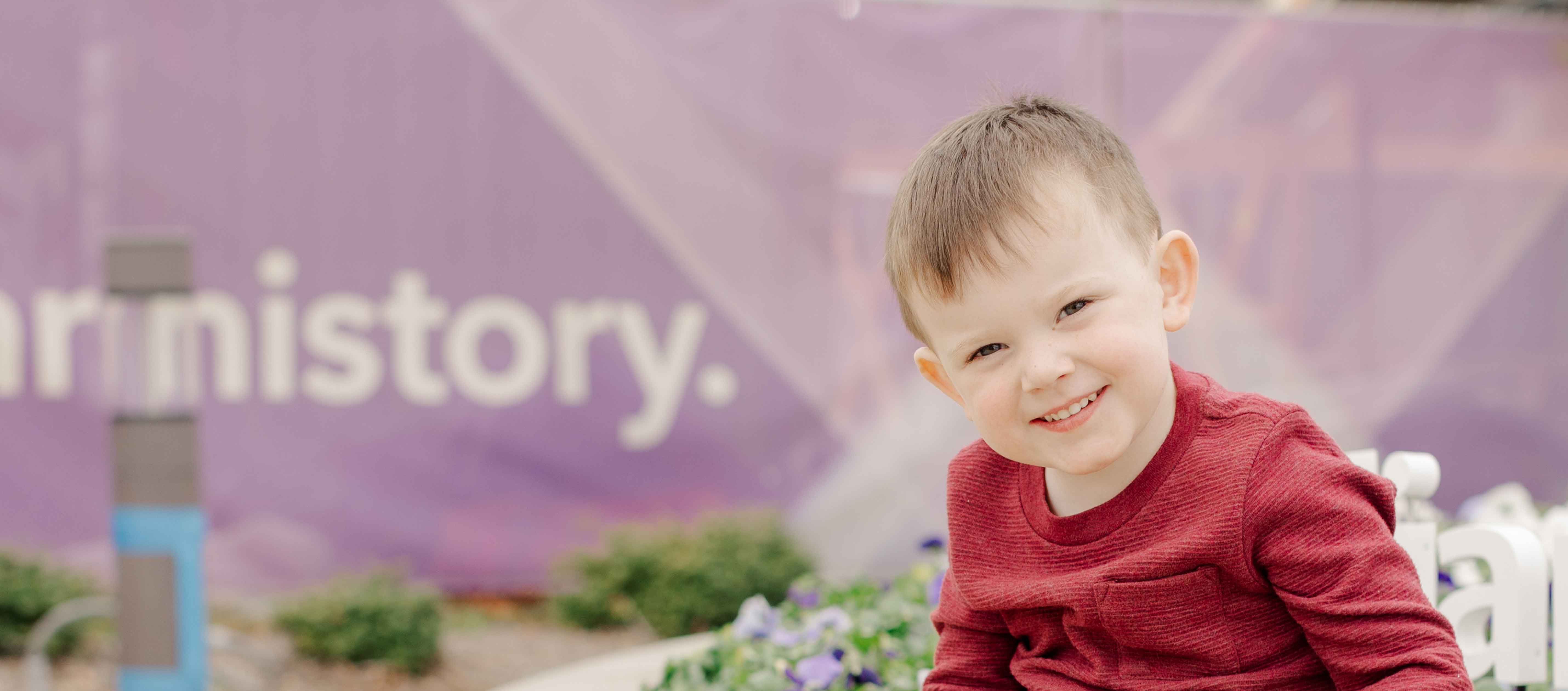 Smiling boy sitting outside hospital wearing red shirt.