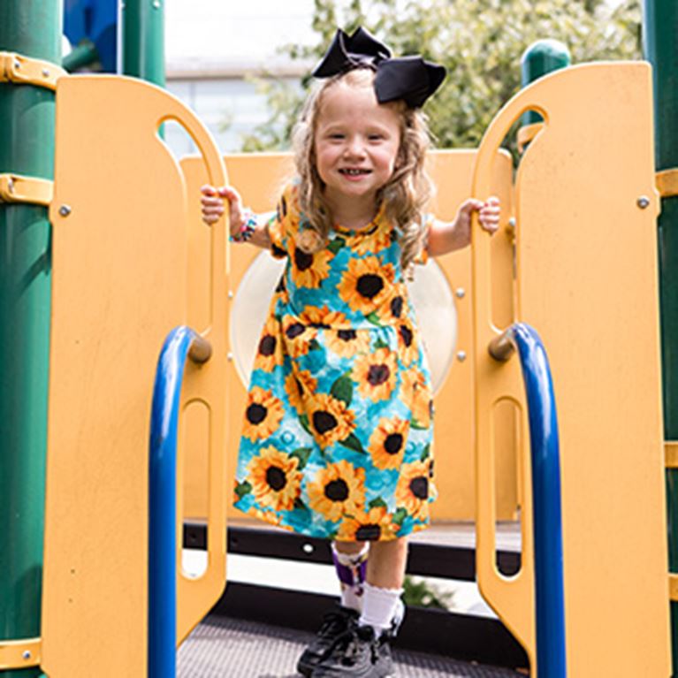 Girl on playset wearing sunflower dress.