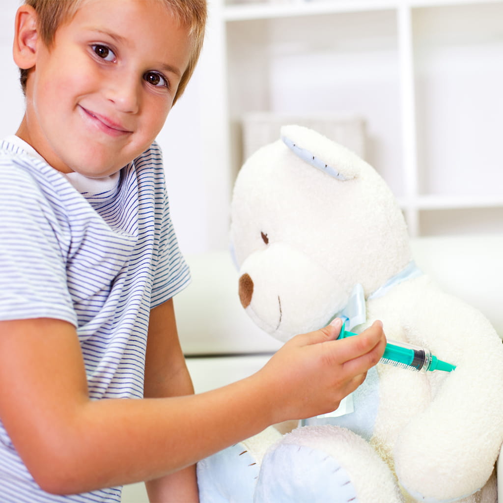 Child pretending to vaccinate teddy bear.