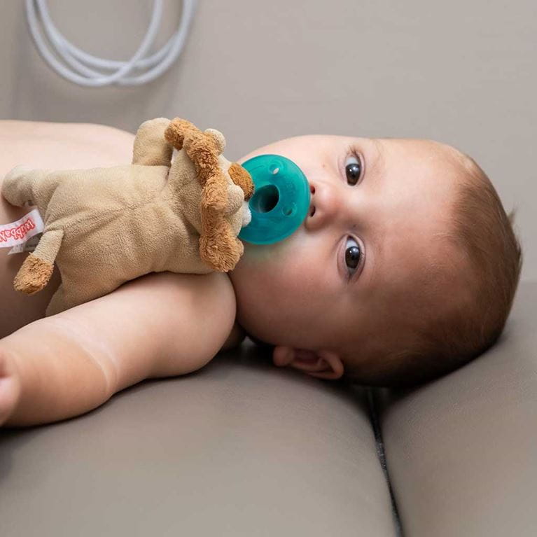 Baby lying down with pacifier in mouth.