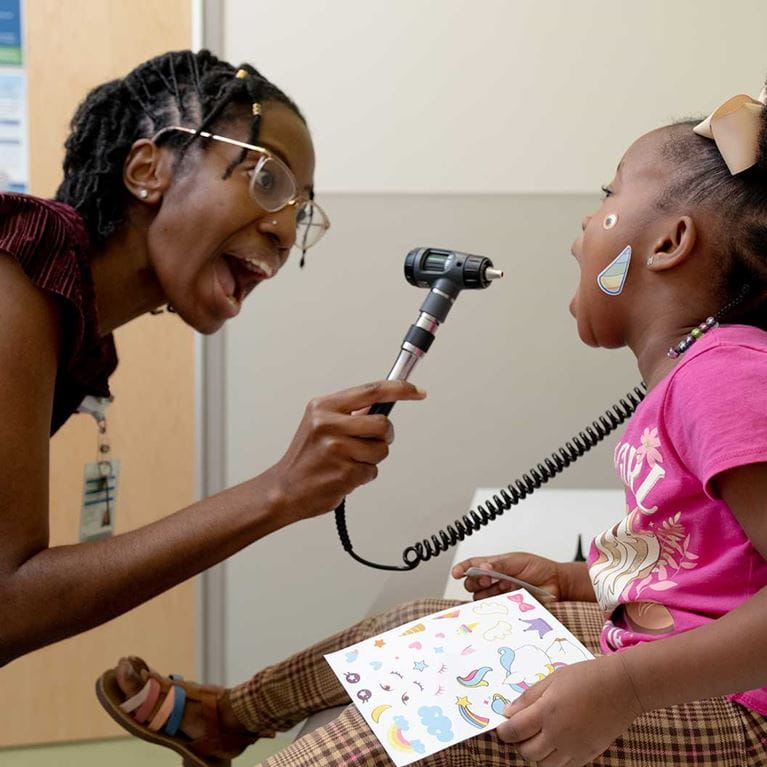 Female doctor looking at the throat of a toddler girl.