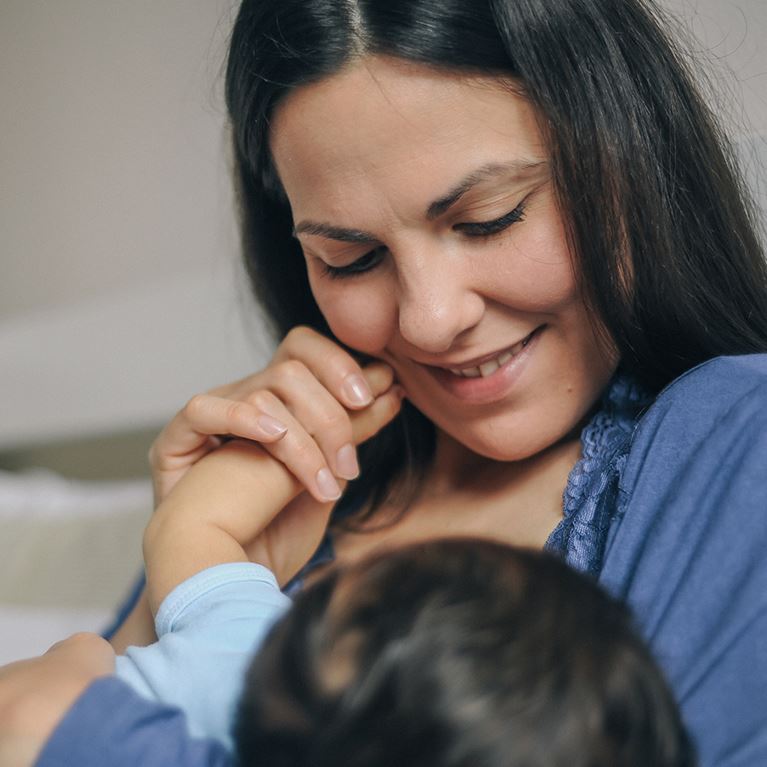 Mom holding baby's hand while breastfeeding.
