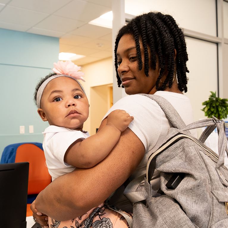 Mom with backpack holding little girl on her hip.