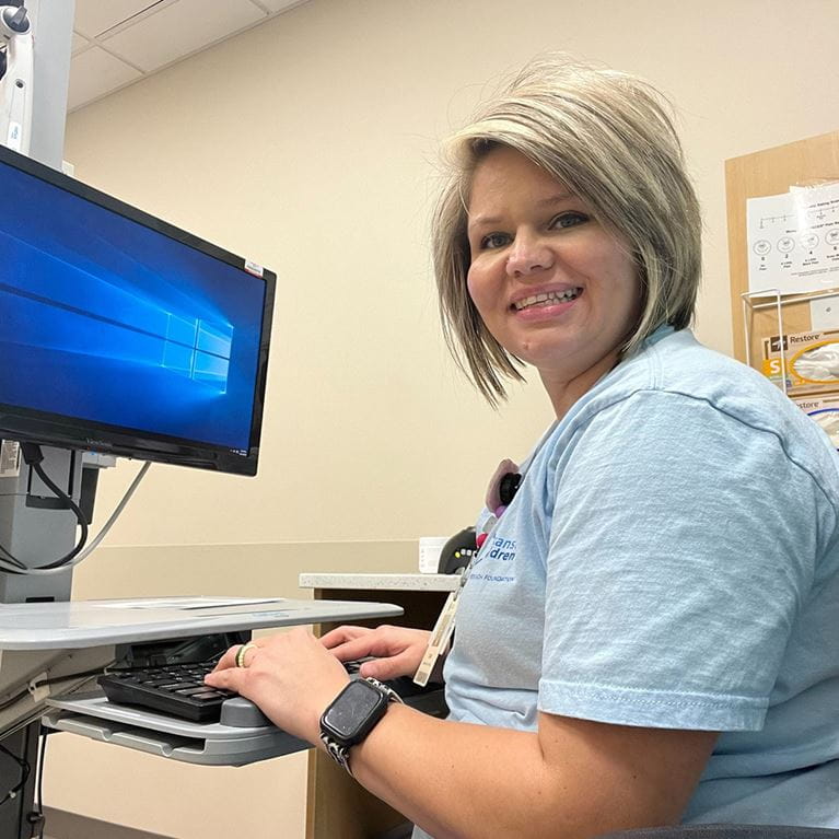 Female employee in light blue t-shirt sitting at computer desk.