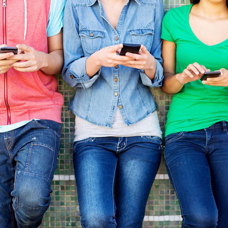 Three teenagers standing while scrolling through phones.