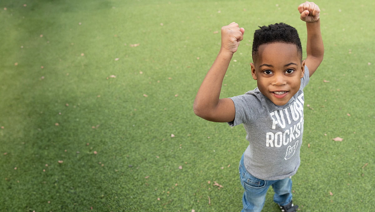 Young boy at the park posing with arms in the air.