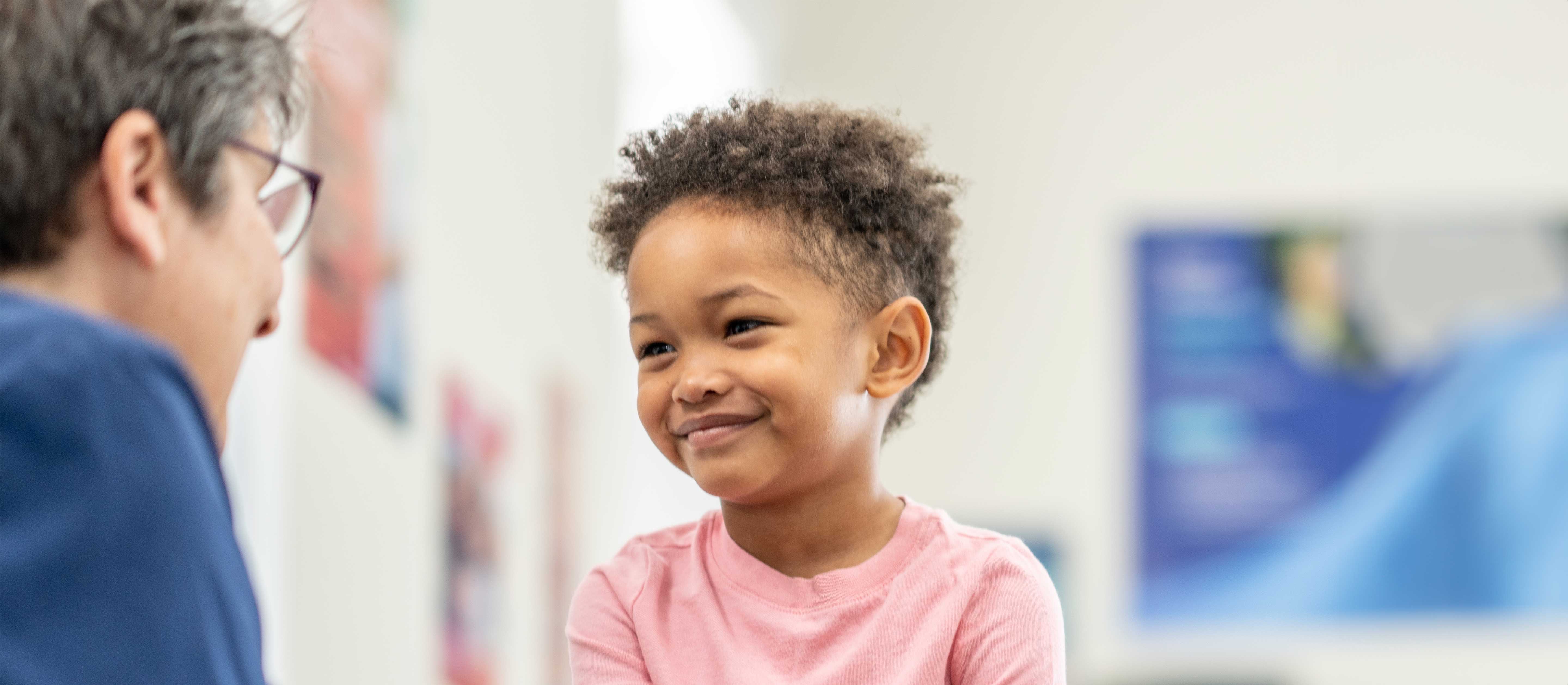 Little boy in pink shirt smiling at nurse while in clinic.