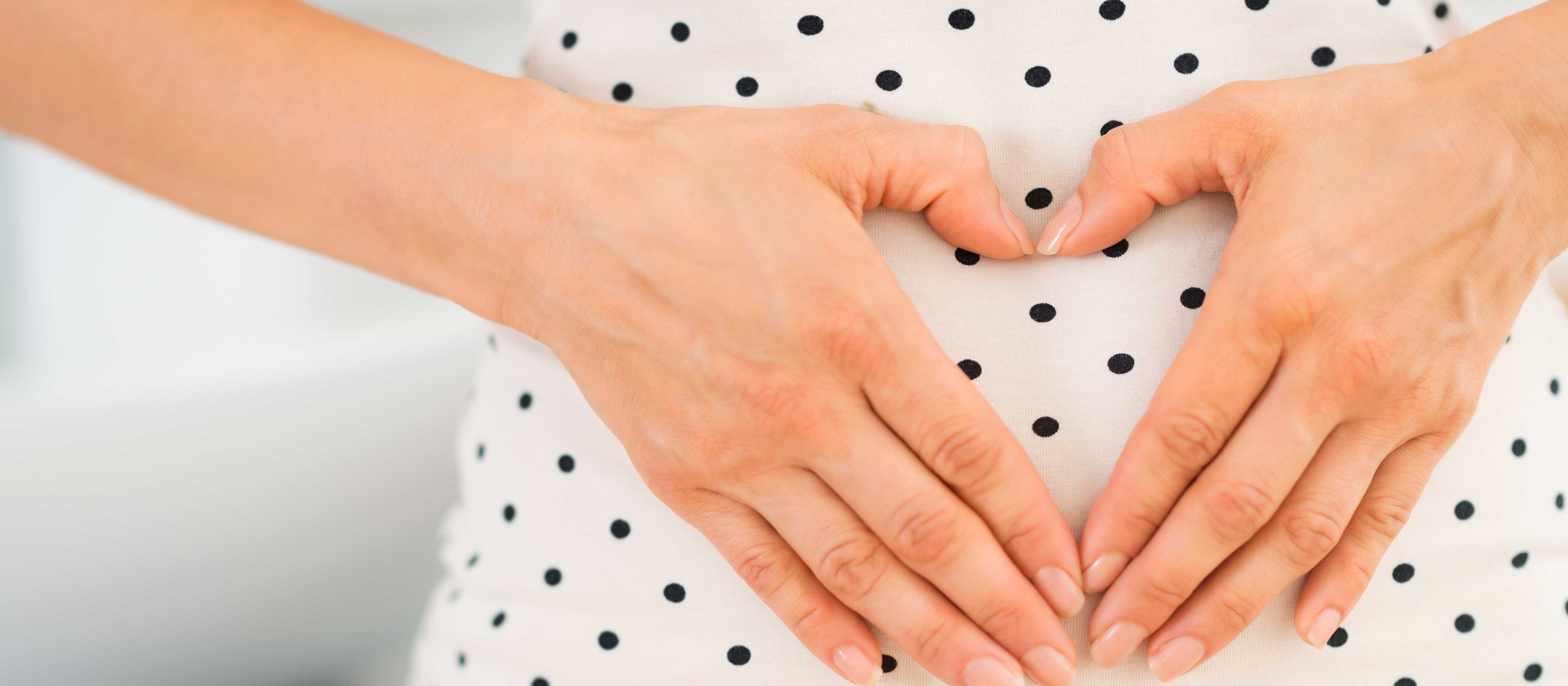 Pregnant woman with heart shaped hands on belly