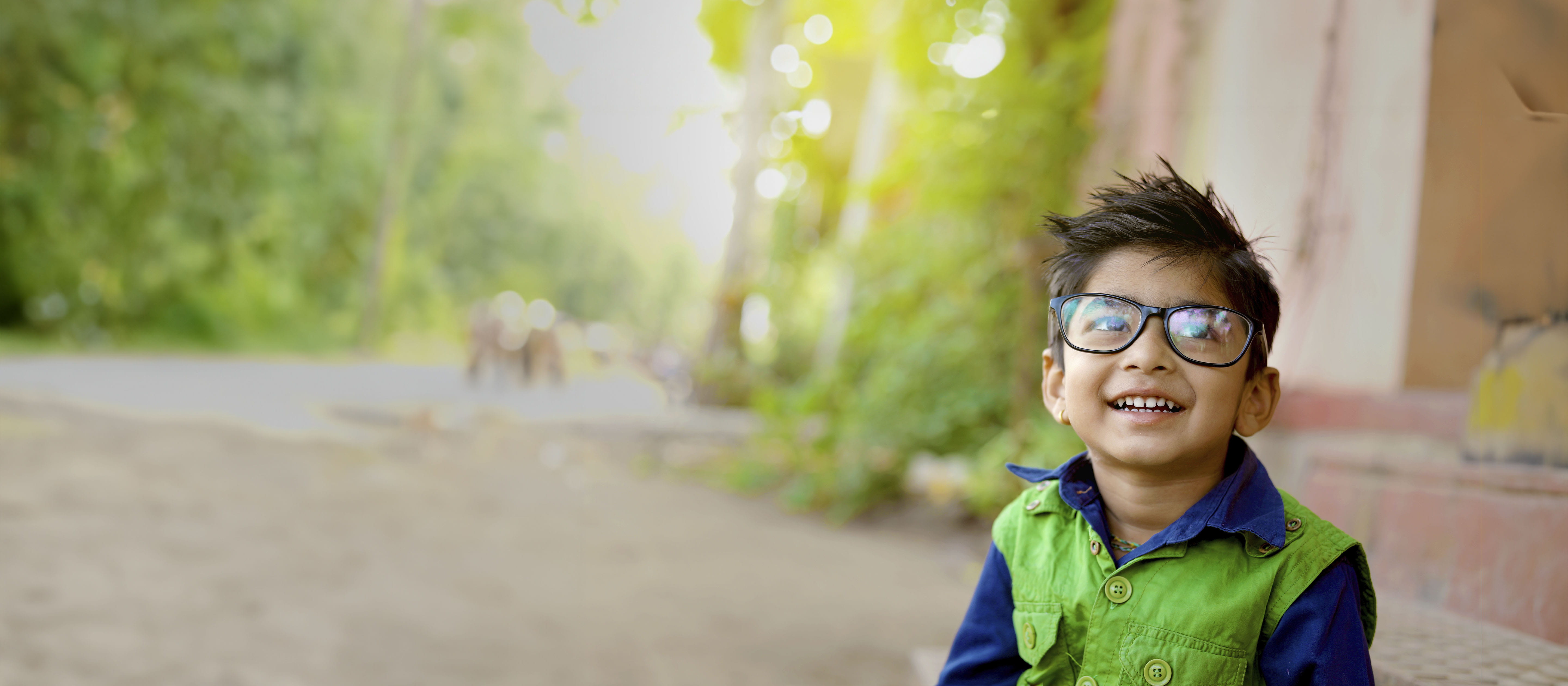 Smiling boy wearing blue and green wearing glasses.