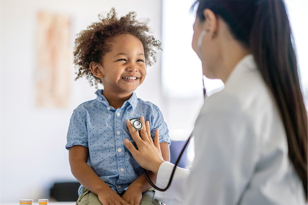 Doctor using stethoscope on smiling male toddler.