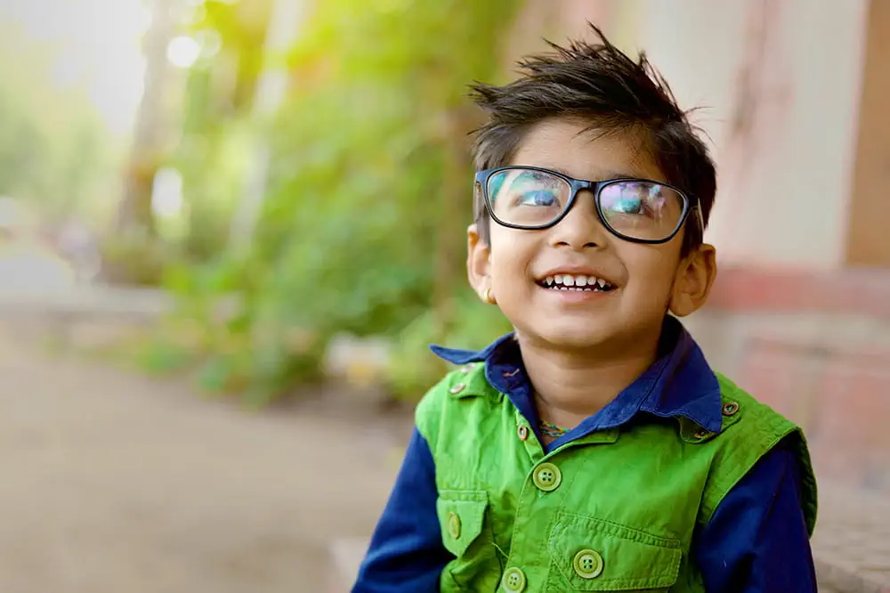 Niño con gafas con camisa azul y verde afuera.
