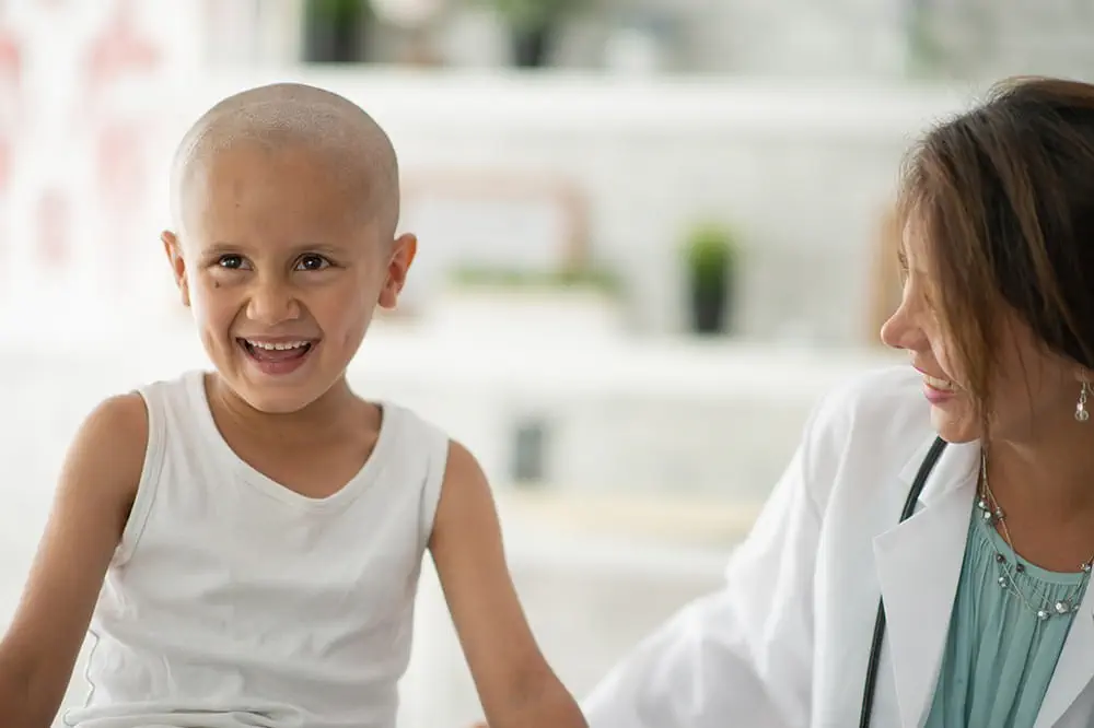 Bald child smiling while sitting with doctor.