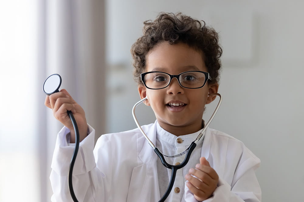 Niño pequeño con bata blanca sosteniendo un estetoscopio.