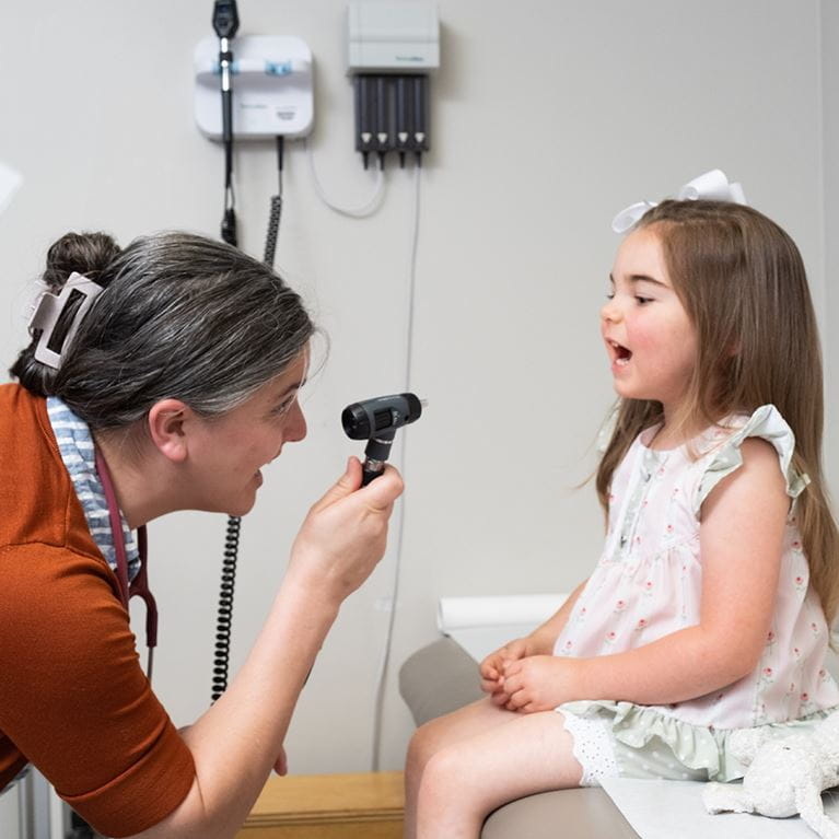 Doctor looking at throat of female patient in clinic room. 