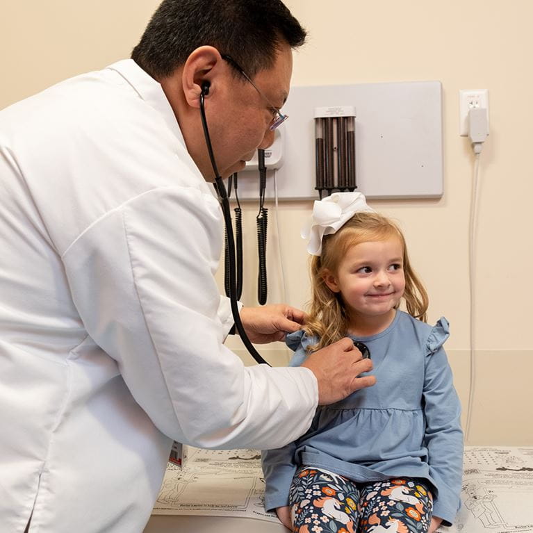 Male doctor wearing white coat using stethoscope on female patient.