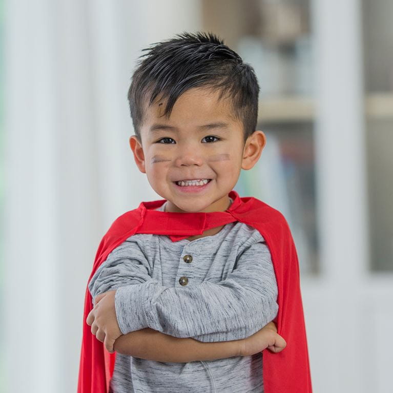 Niño en el pasillo sonriendo y vistiendo capa roja