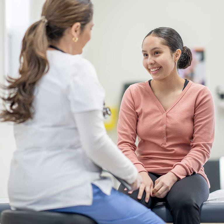 Adolescent girl in clinic speaking with physician.