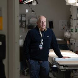 Dr. Stanford standing in emergency department room with hand resting on hospital bed.