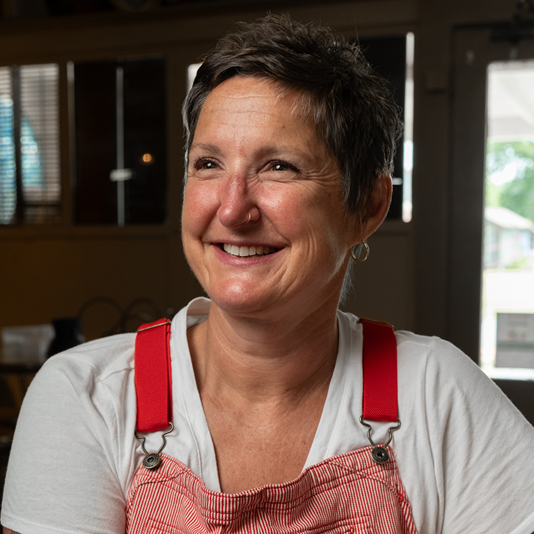 Smiling woman wearing white shirt and red overalls.