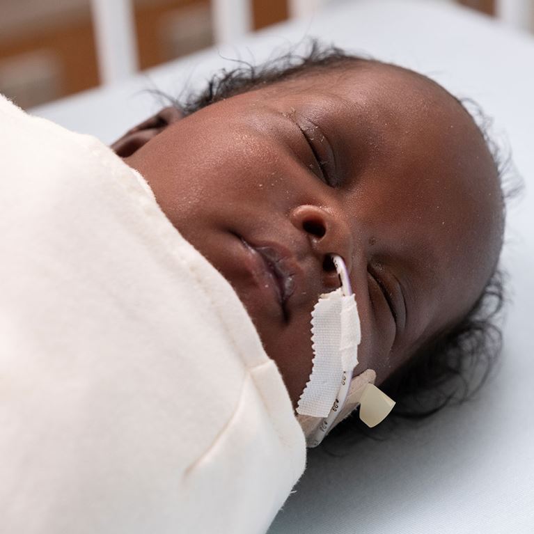 Sleeping NICU baby swaddled in white blanket.