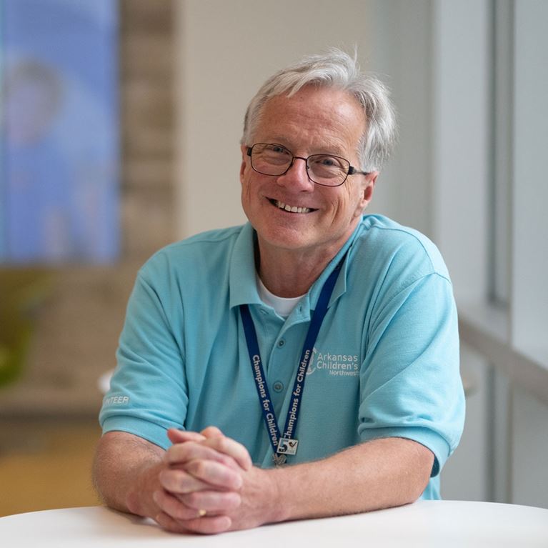 Smiling male volunteer sitting at white table with hands together.