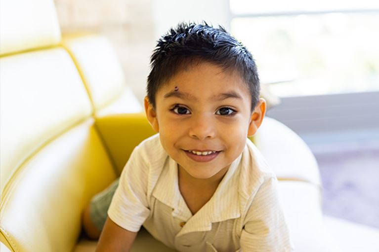 Little boy with dark hair wearing yellow shirt smiling at camera.