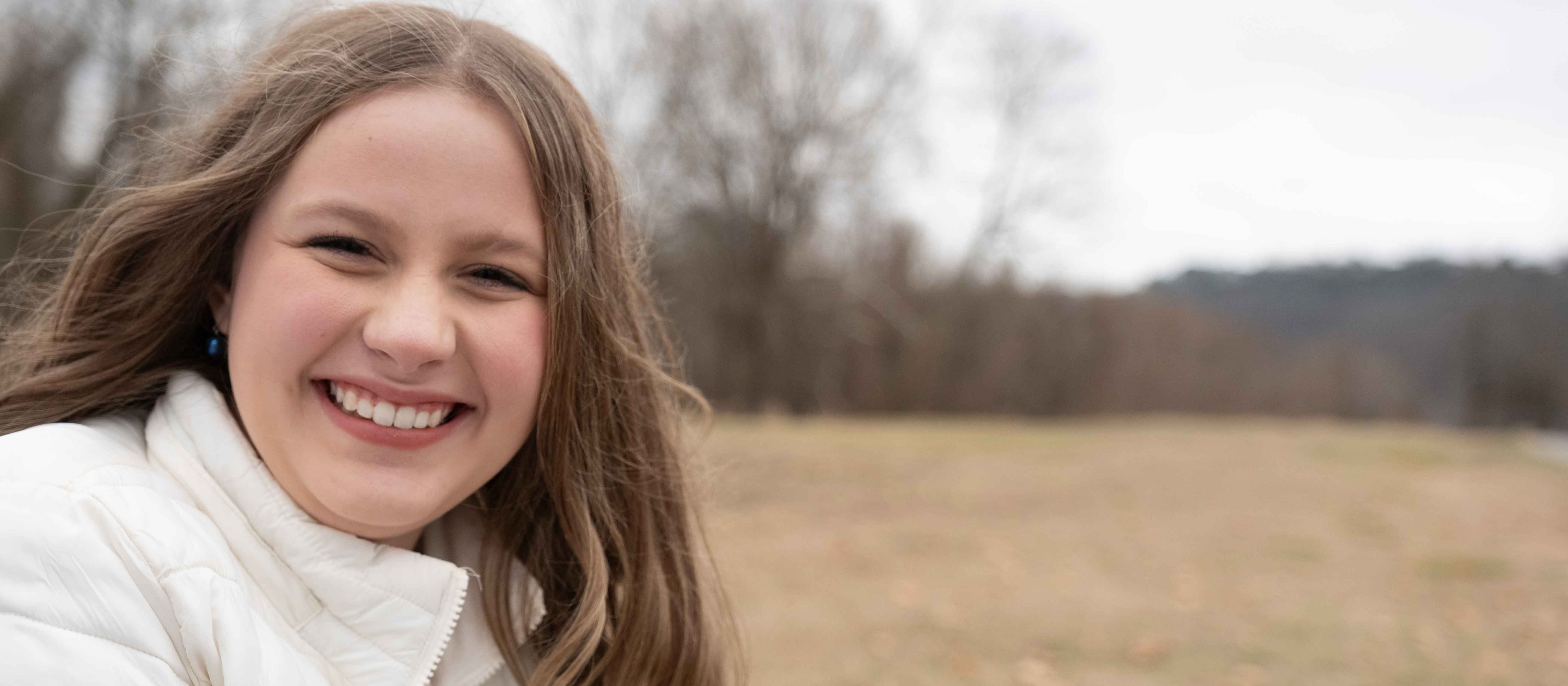 Smiling teenage girl outside wearing white coat.