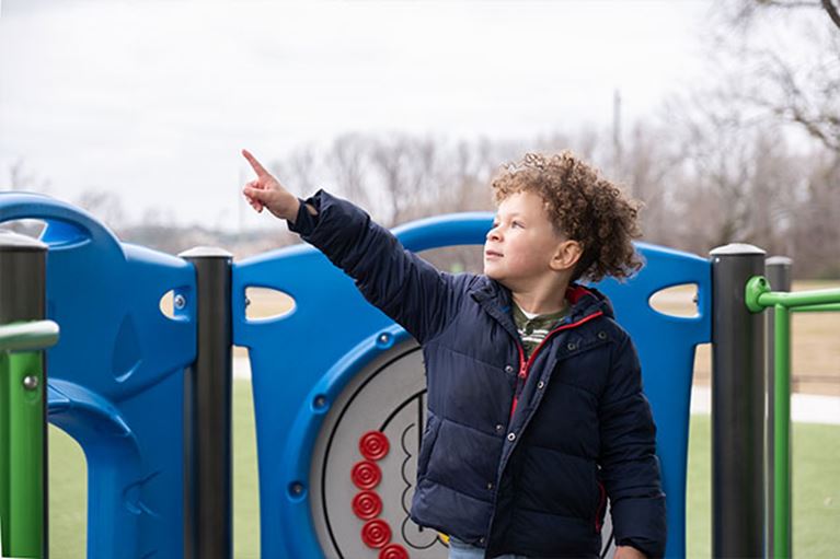 Young boy wearing blue coat playing outside on cloudy day.