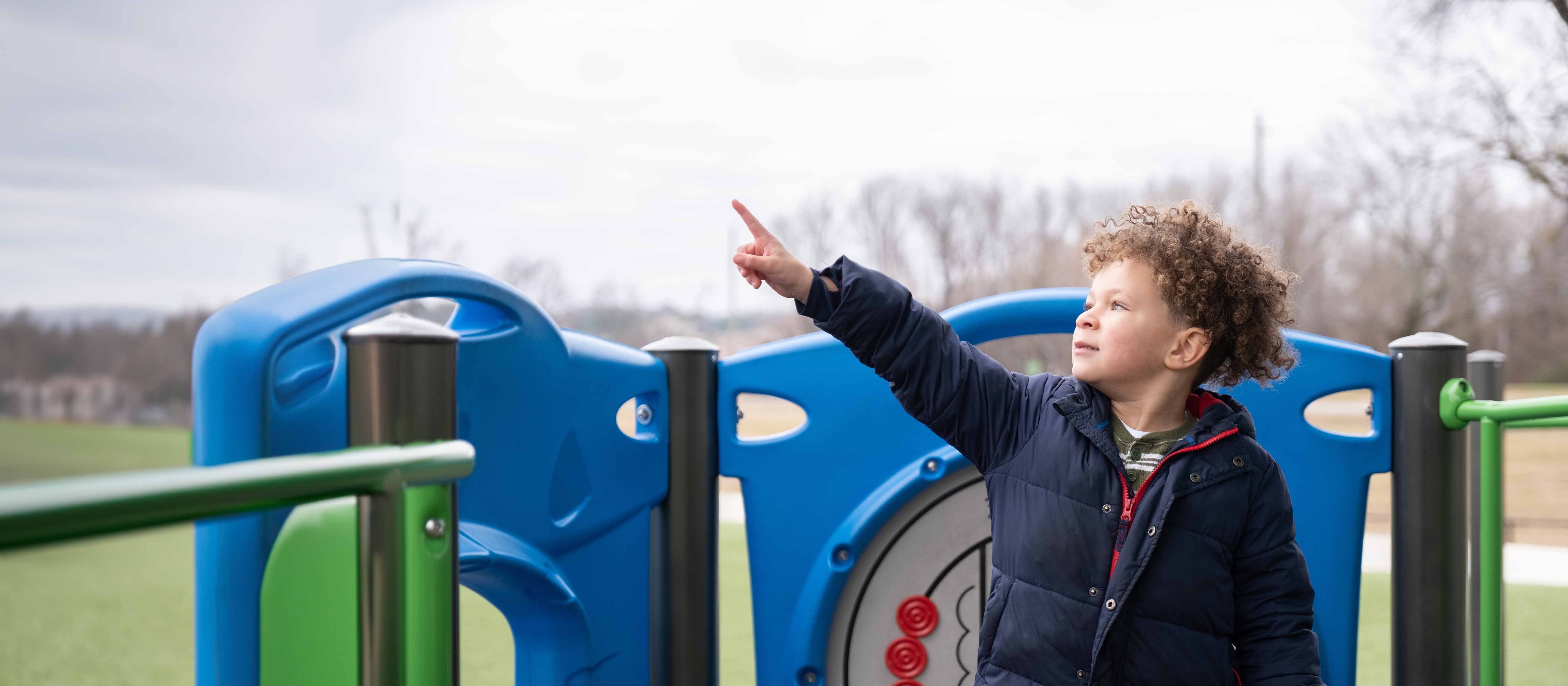Young boy wearing blue coat playing outside on cloudy day.