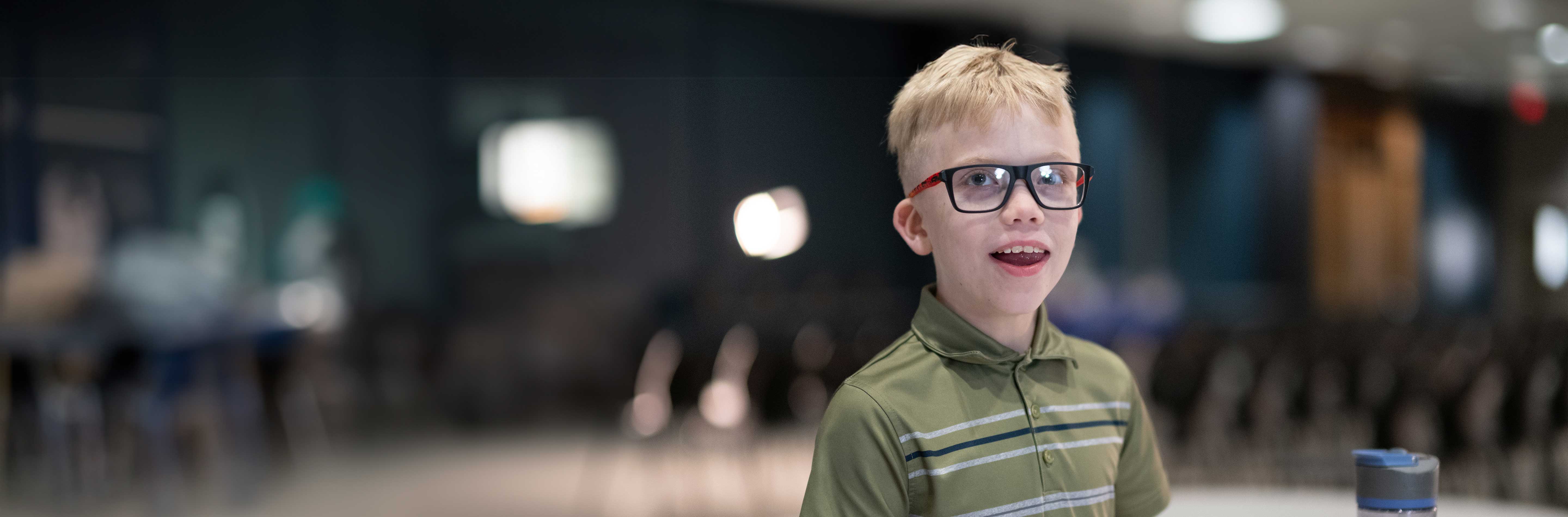 Smiling boy with blonde hair wearing a green shirt and eyeglasses.