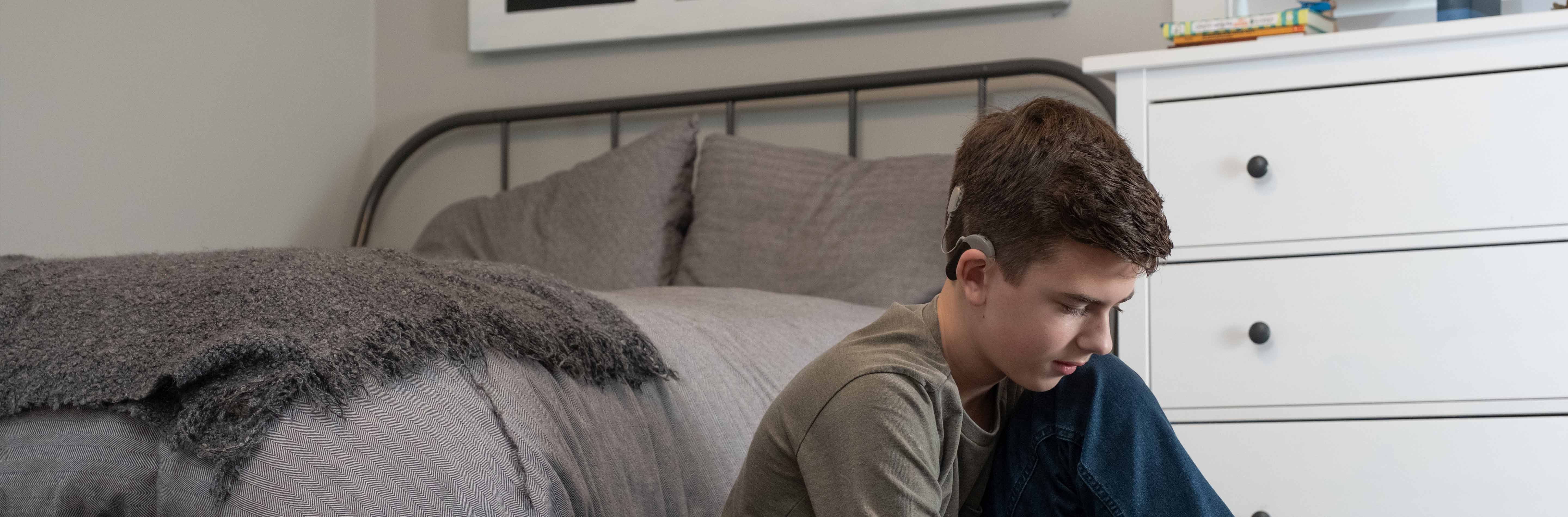 Teenage boy sitting on bedroom floor tying his shoes.