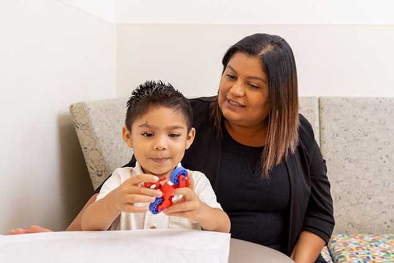 Mother watching boy play with toy in waiting room.