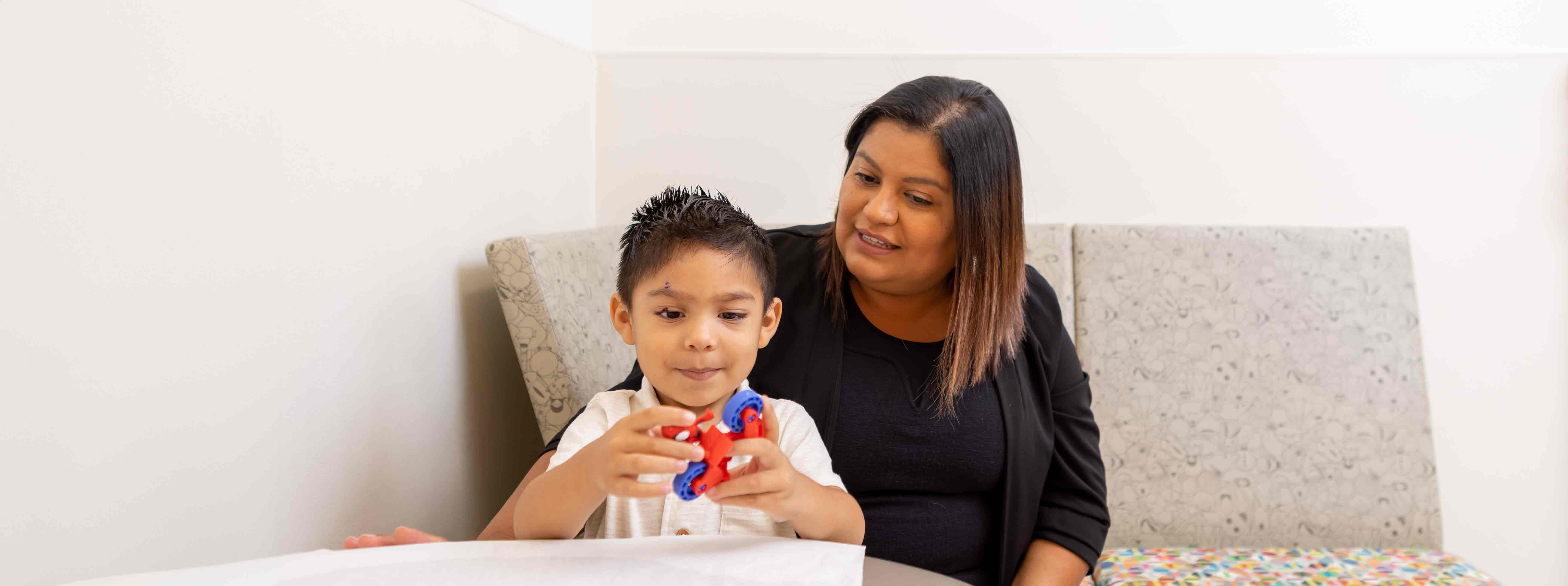 Mother watching boy play with toy in waiting room.