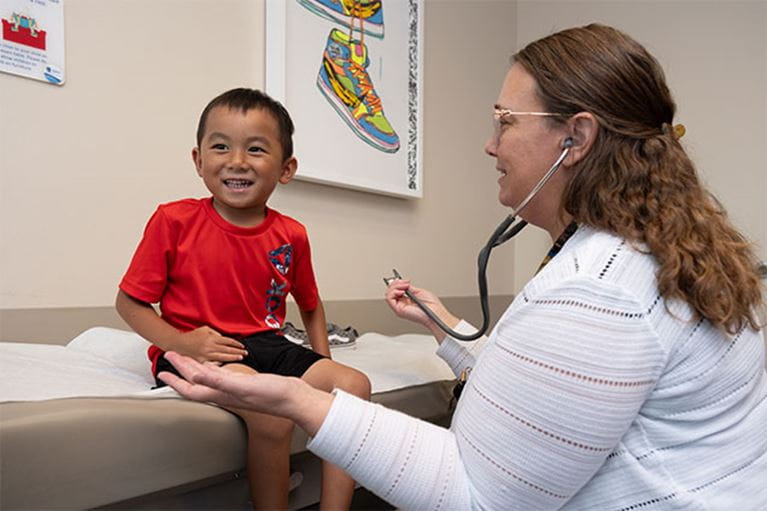 Young Asian boy wearing red shirt being checked by doctor in clinic.