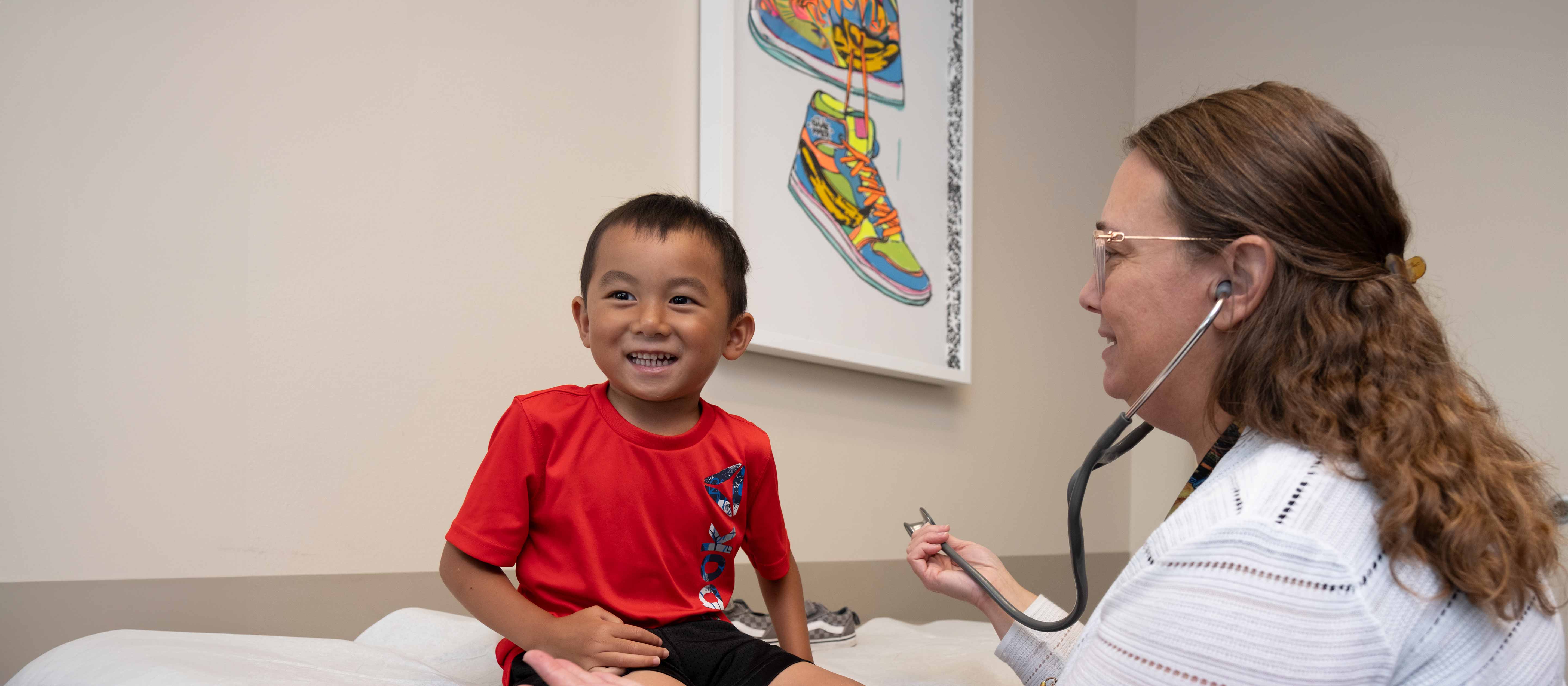Young Asian boy wearing red shirt in clinic room being checked by doctor.
