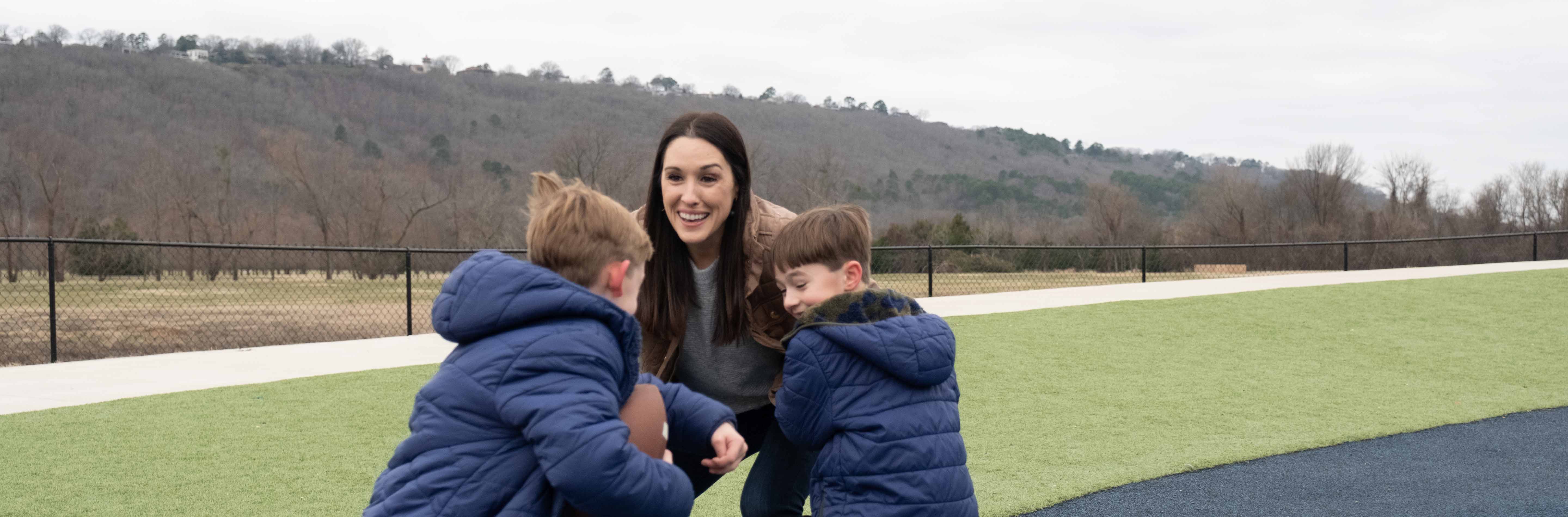 Mom playing football outside with sons in blue coats.