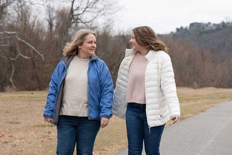 Mom wearing blue jacket walking outside with daughter in white coat. 