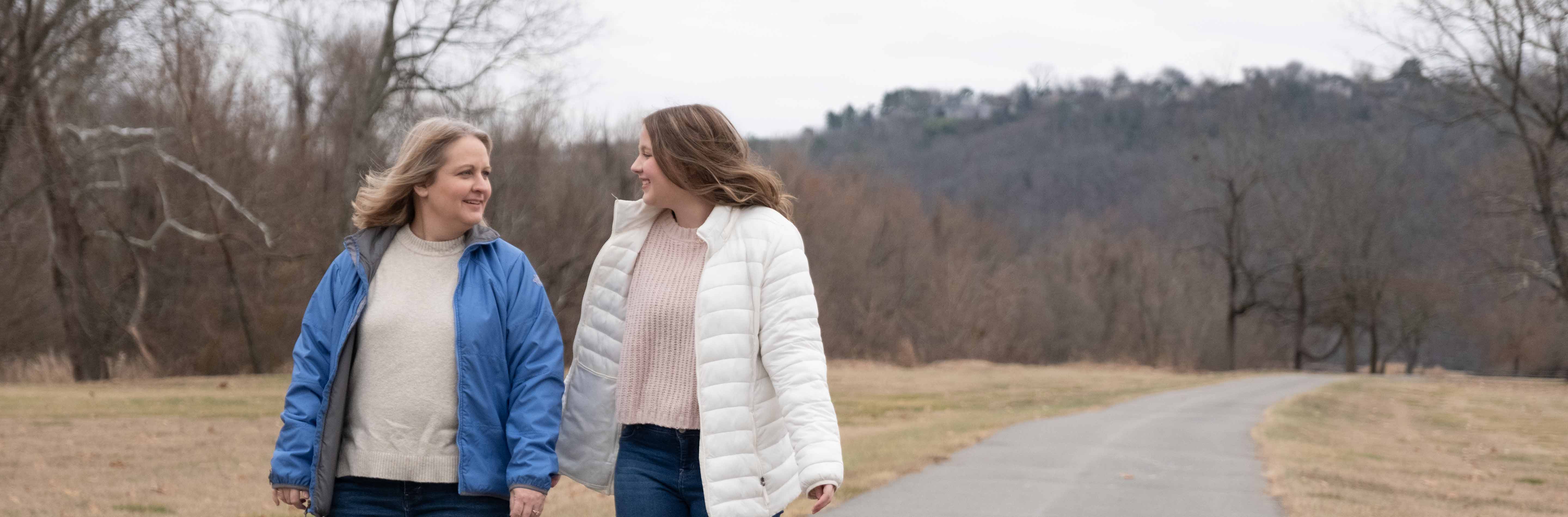 Mom in blue jacket walking outside with teenage daughter in white coat. 