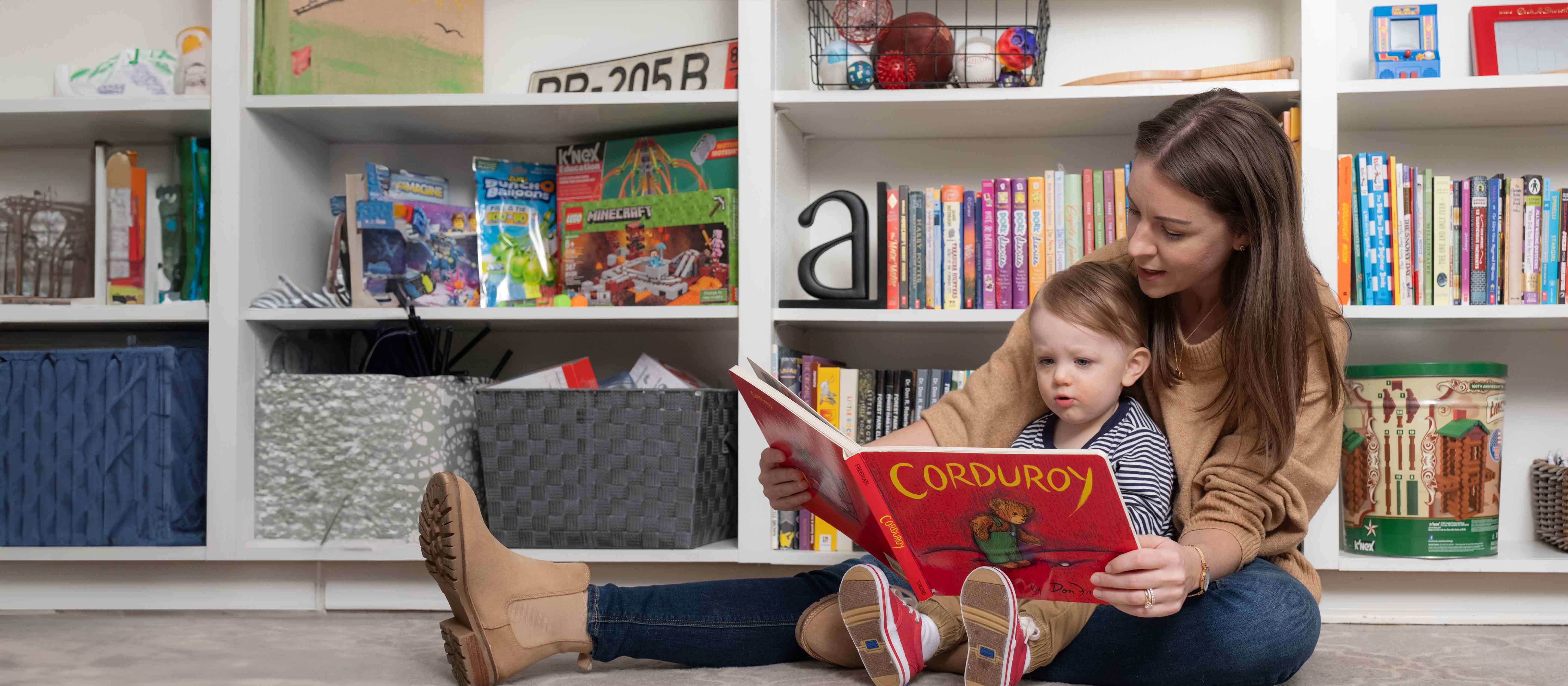 Mom reading a book to son in front of bookshelf.