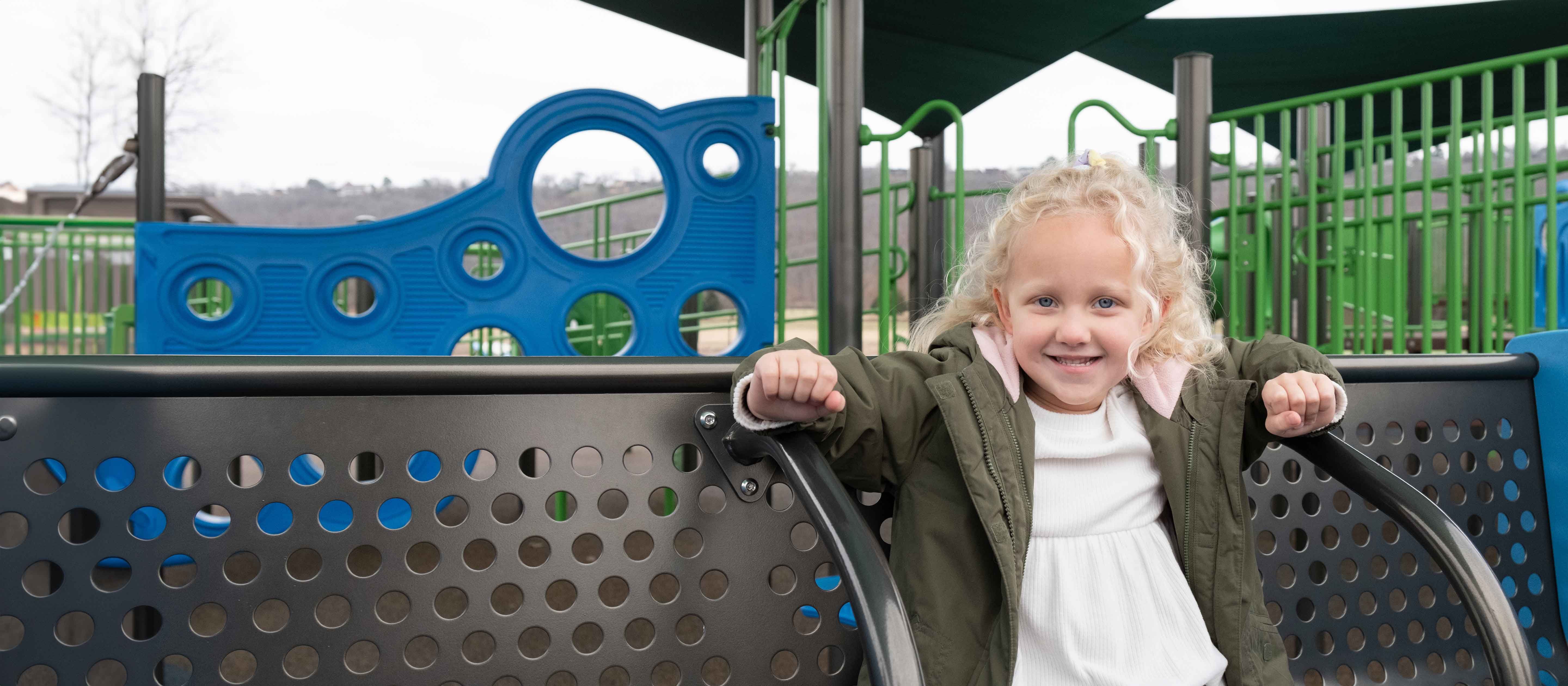 Little girl with curly blonde hair sitting on black bench.
