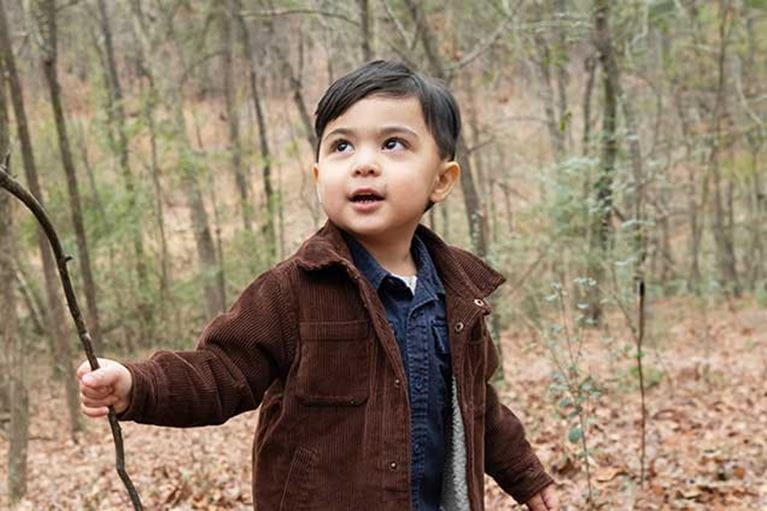 Little boy in brown jacket playing with a stick in the woods.