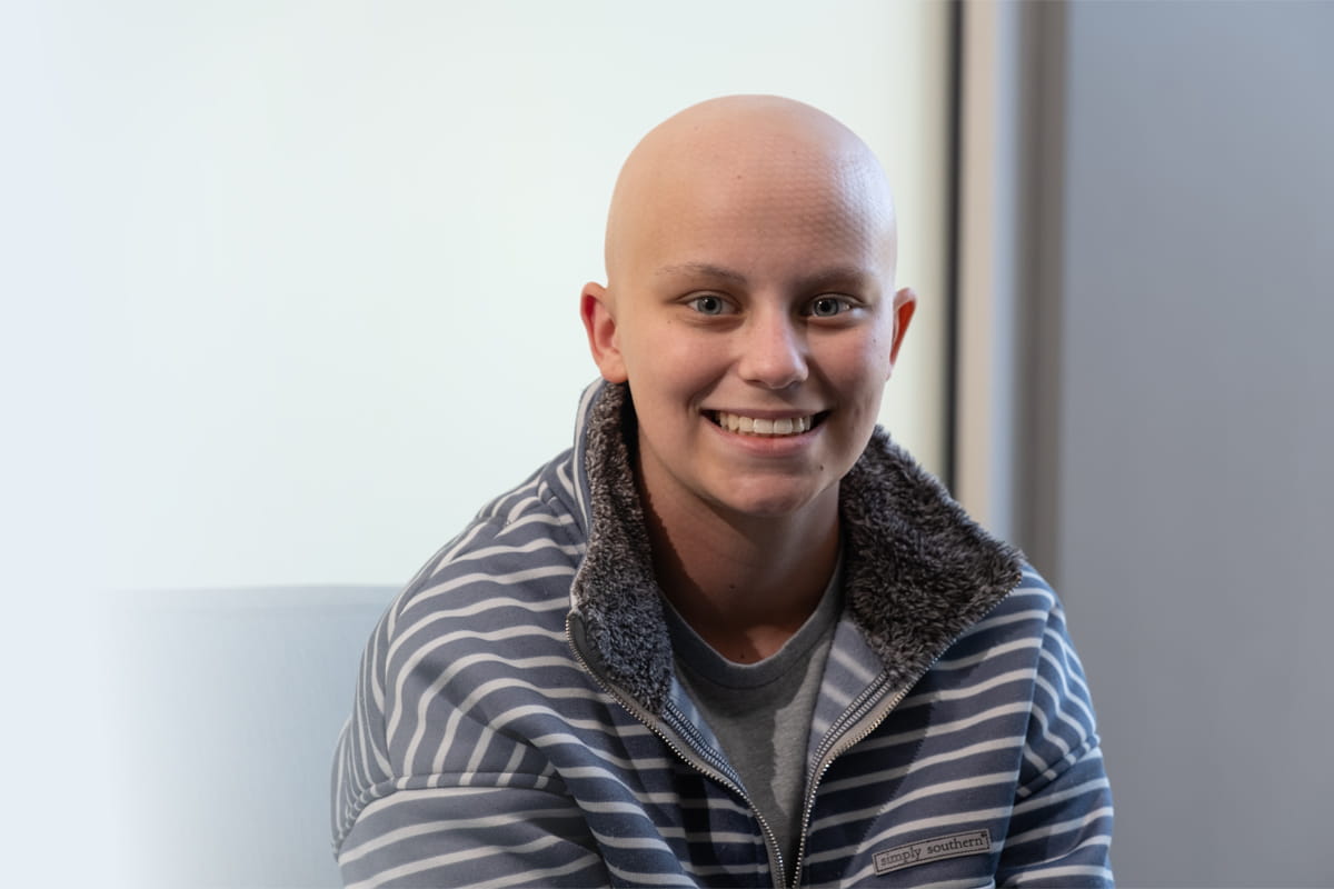 Smiling female cancer patient wearing gray sweater with white stripes.