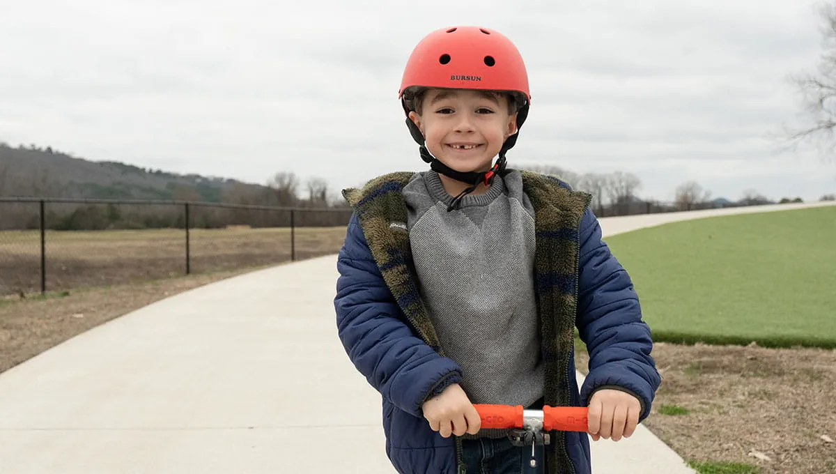 Male patient riding scooter wearing red helmet and blue coat.