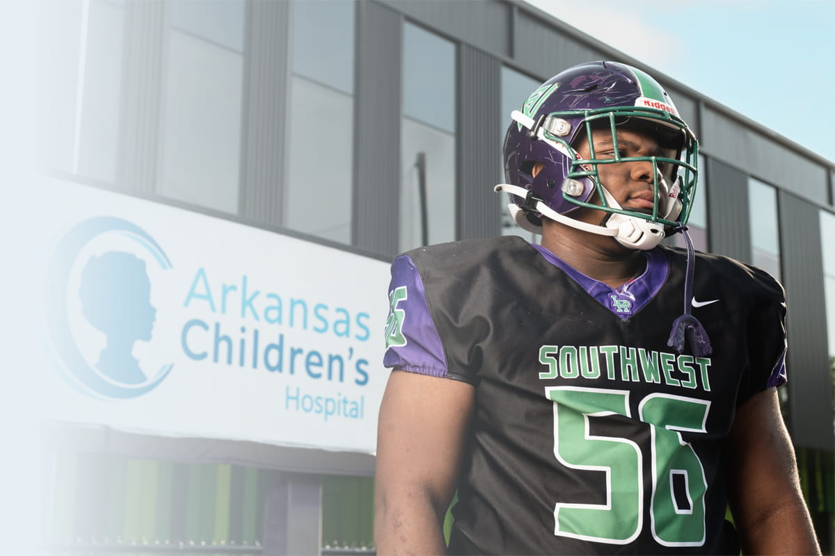 A football player in a black jersey with "SOUTHWEST" and the number 56 stands in front of the Arkansas Children's Hospital sign.