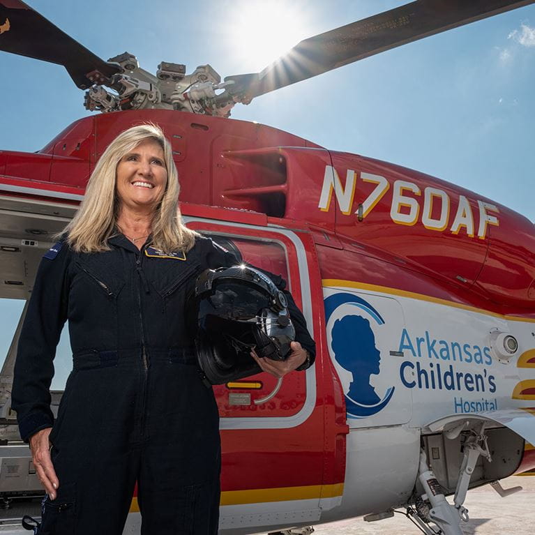 Arkansas Children's flight nurse standing beside red helicopter.