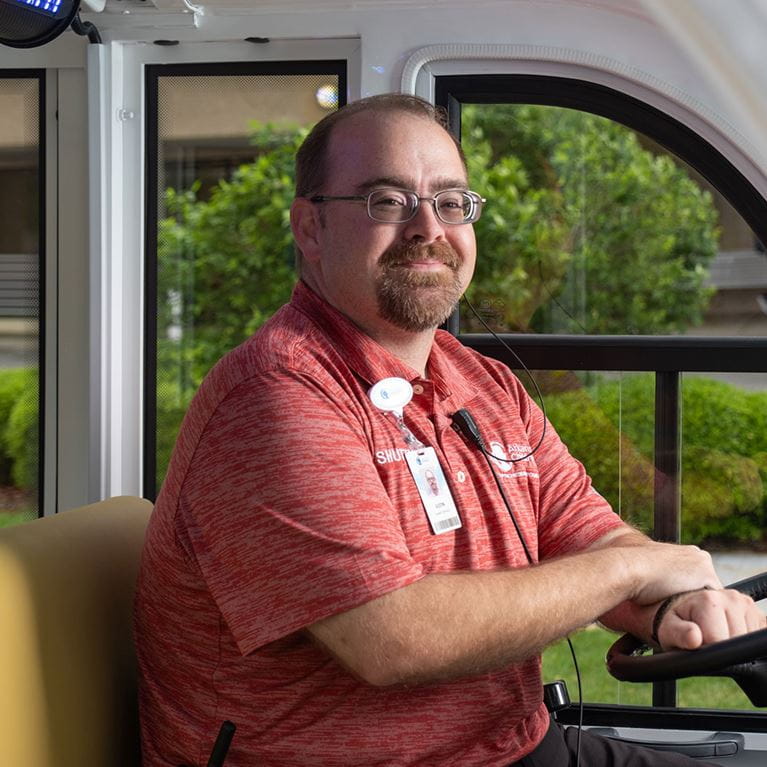 Male in red polo shirt driving hospital shuttle.