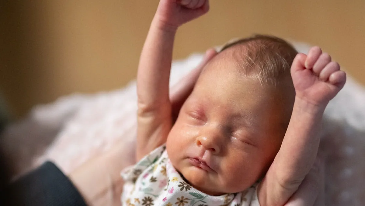 Newborn baby stretching with arms above head.