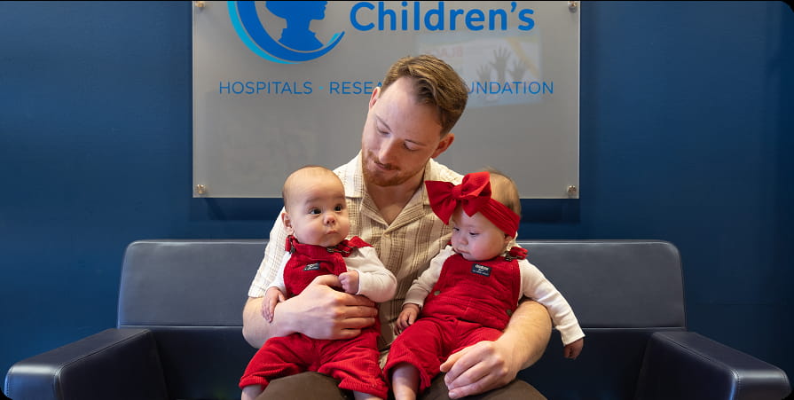 Dad holding twins wearing red outfits.